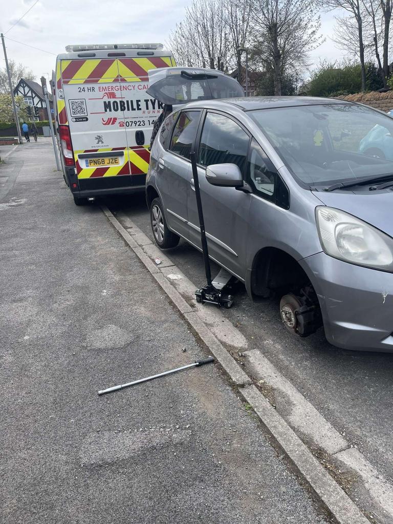 Car jacked up at the kerb with its wheel removed for a puncture repair, Mobile Tyre Runner van behind
